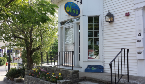 Exterior of a building with a sign reading "Olive," featuring a stone staircase and colorful flower beds.
