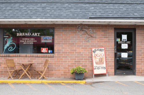 Exterior of Bread Art bakery with a sign reading "OPEN," featuring a small table and chairs outside.