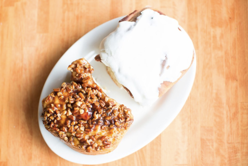 A plate with two cinnamon rolls: one topped with cream frosting and the other with a pecan caramel glaze.