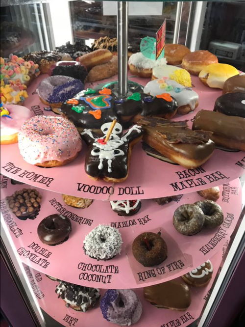 A colorful display of various donuts, including sprinkles, chocolate, and unique themed designs, on a pink background.