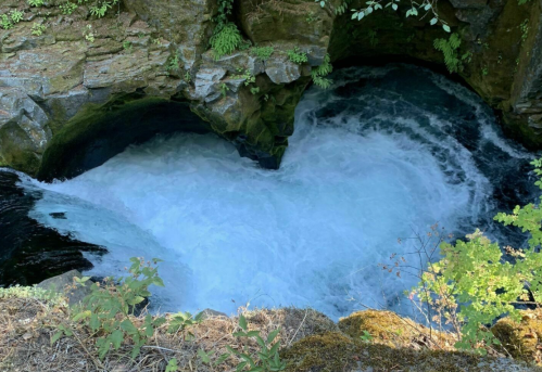 A rushing river cascades over rocks, creating a heart-shaped pool surrounded by lush greenery.