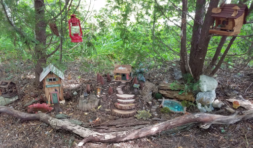 A whimsical miniature fairy garden with tiny houses, lanterns, and a winding path among trees and natural elements.