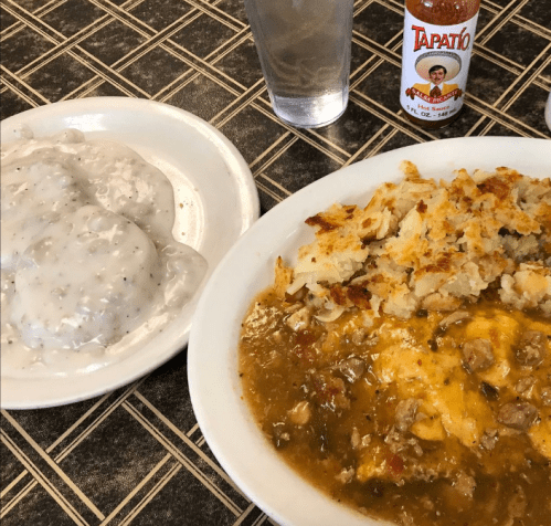 A plate of hearty casserole with meat and vegetables, served with biscuits and gravy, alongside a bottle of hot sauce.