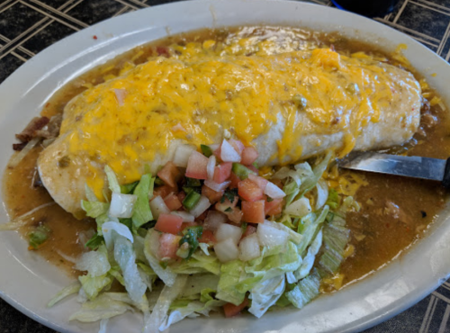A large cheese-covered burrito on a plate, served with lettuce and diced tomatoes in a savory sauce.