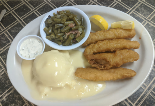 A plate of fried fish fillets with creamy sauce, green beans, a lemon wedge, and a side of tartar sauce.