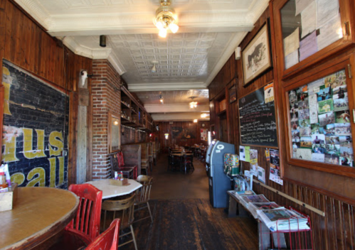 Cozy restaurant interior with wooden decor, red chairs, and a vintage vibe, featuring a long hallway and tables.