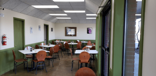 Interior of a restaurant with empty tables and chairs, green walls, and a large mirror on the wall.