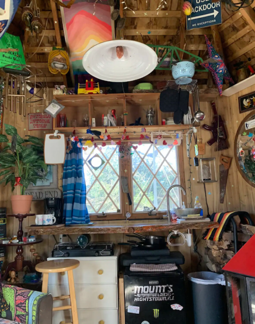 Cozy interior of a rustic shed with colorful decor, a window, kitchen items, and various hanging decorations.
