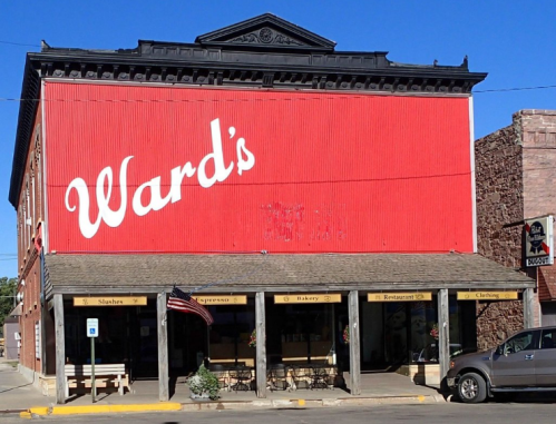 A red building with "Ward's" painted on it, featuring a bakery, restaurant, and clothing store on the ground floor.