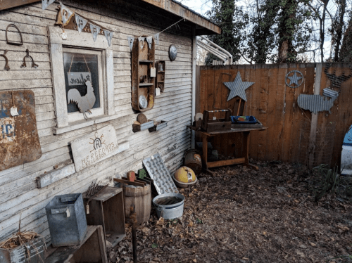 A rustic outdoor space with wooden walls, vintage decor, and various tools scattered among fallen leaves.
