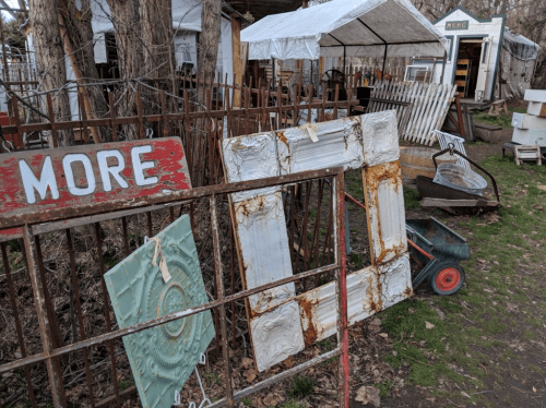 A rustic outdoor market scene featuring vintage items, including a weathered frame and a sign that says "MORE."