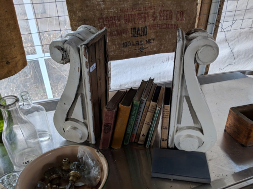 Two decorative bookends holding vintage books, with various items and a burlap sack in the background.