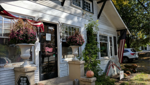 Charming white house with flower pots, pumpkins, and an American flag, welcoming visitors with a sign that says "We are glad you are here."