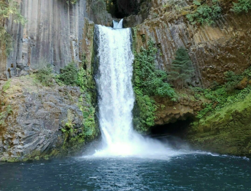 A stunning waterfall cascades down rocky cliffs into a serene pool, surrounded by lush greenery.