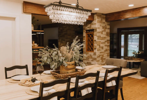 A stylish dining area featuring a wooden table, elegant chandelier, and a centerpiece of greenery.