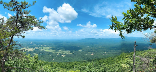 A panoramic view of lush green mountains and valleys under a bright blue sky with fluffy white clouds.