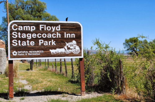 Sign for Camp Floyd Stagecoach Inn State Park, featuring a wooden design and surrounded by greenery and blue skies.