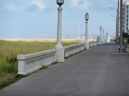 A scenic walkway lined with lamp posts, leading towards a grassy area and a distant American flag.
