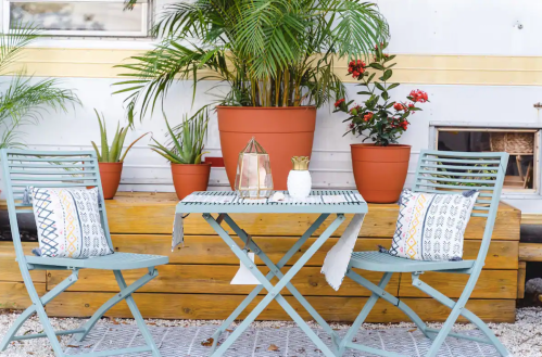 A cozy outdoor seating area with a small blue table, two chairs, and potted plants in a bright, inviting space.