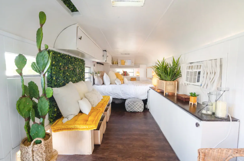 Cozy interior of a renovated trailer with a bed, seating area, plants, and bright decor.