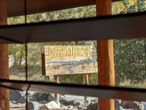 Sign for Feather River Motel, featuring a scenic illustration and surrounded by trees and rocks. View through blinds.