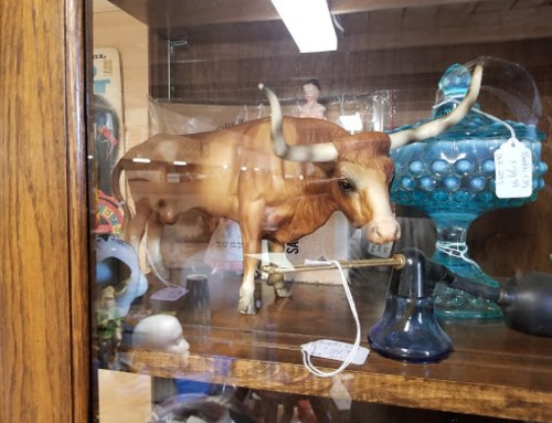 A glass display case containing a toy longhorn steer and various collectibles, including a blue glass piece and a bell.