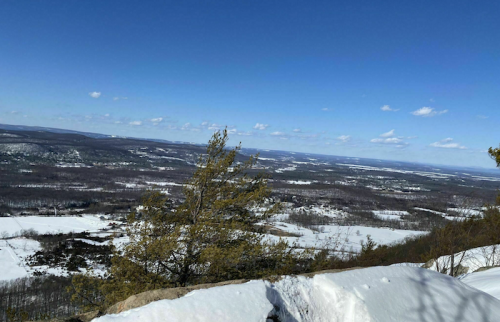 A panoramic view of a snowy landscape with rolling hills and a clear blue sky dotted with clouds.