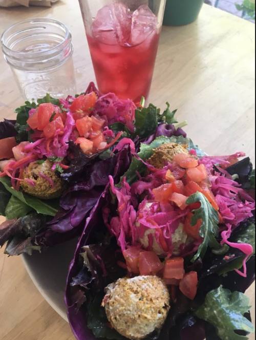 Two vibrant salads with lettuce wraps, topped with tomatoes, pink cabbage, and falafel balls, alongside a glass of iced drink.