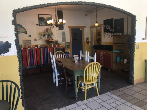 Cozy café interior with colorful chairs, a wooden table, and vibrant decor, featuring an archway and artwork on the walls.