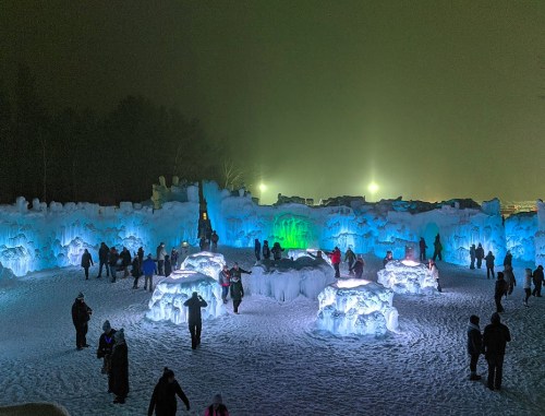 A winter scene featuring illuminated ice sculptures and people exploring a snowy landscape at night.