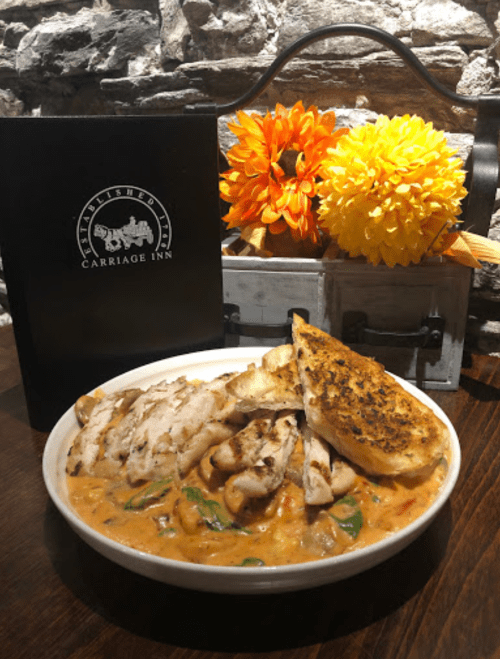 A bowl of creamy chicken pasta with grilled chicken, spinach, and garlic bread, set against a rustic backdrop.
