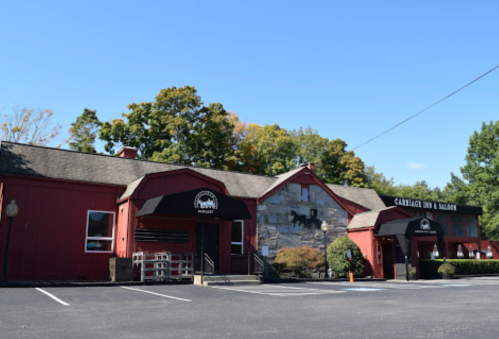 Red barn-style building with stone accents, featuring a sign for "Carriage Inn & Balloons" and a parking lot.