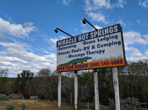 Sign for Miracle Hot Springs featuring swimming, dome lodging, private pools, RV camping, and massage therapy. Open year-round.