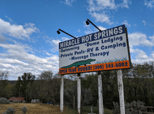 Sign for Miracle Hot Springs featuring swimming, dome lodging, private pools, RV camping, and massage therapy. Open year-round.