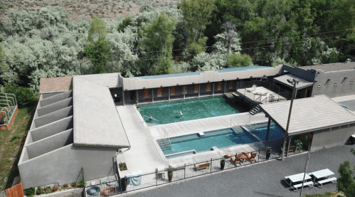 Aerial view of a modern swimming pool surrounded by greenery, featuring lounge chairs and shaded areas.
