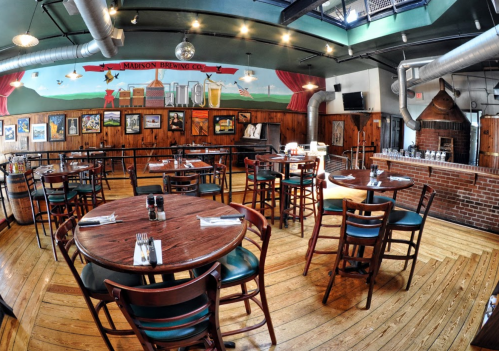 Interior of a rustic restaurant with wooden tables, chairs, and a mural depicting a cityscape on the wall.