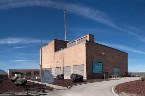 A large brick building with a sign reading "EBBM" against a clear blue sky, surrounded by rocky terrain.