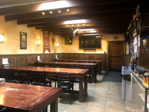 Interior of a restaurant featuring wooden tables, chairs, and a TV on the wall, with warm lighting and a cozy atmosphere.