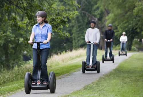 A group of four people riding Segways on a grassy path in a park.