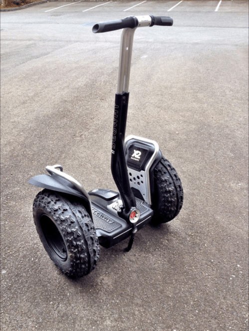 A black and silver electric scooter with large, rugged tires parked on a paved surface.