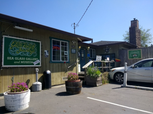 A quaint building with signs for a sea glass gallery and museum, featuring flower pots and an open sign.