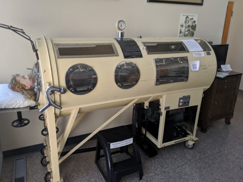A vintage iron lung machine with a mannequin head inside, displayed in a museum setting.