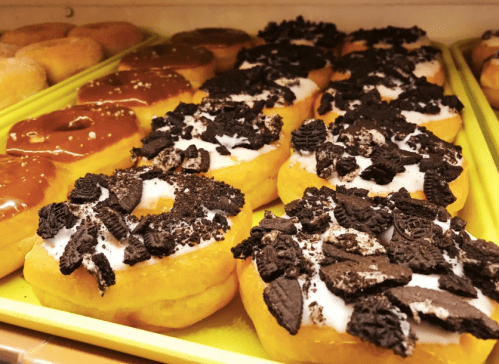 A tray of donuts topped with chocolate icing and crushed Oreo cookies, arranged neatly in a display.