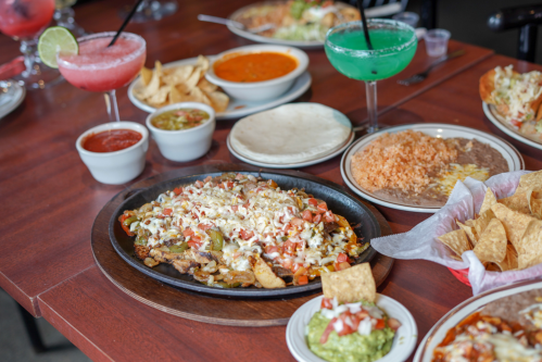 A vibrant spread of Mexican dishes, including sizzling fajitas, guacamole, salsa, rice, and colorful drinks.