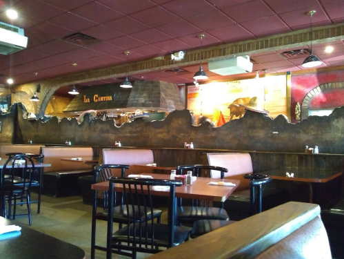 Interior of a restaurant with wooden booths, tables, and a decorative mural on the wall. Warm, inviting atmosphere.