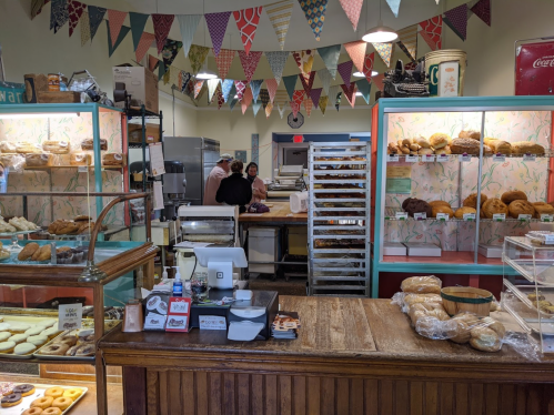 A cozy bakery interior with colorful bunting, displaying various baked goods and a counter with a cash register.