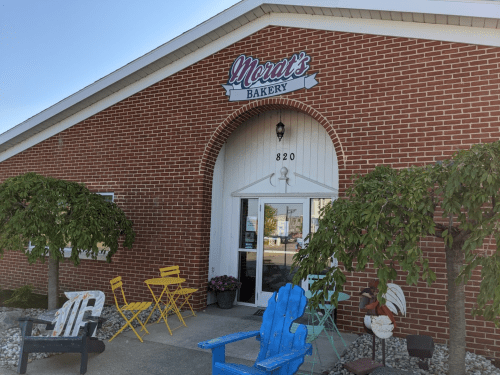 Exterior of Merat's Bakery featuring a brick facade, white door, and colorful outdoor seating.
