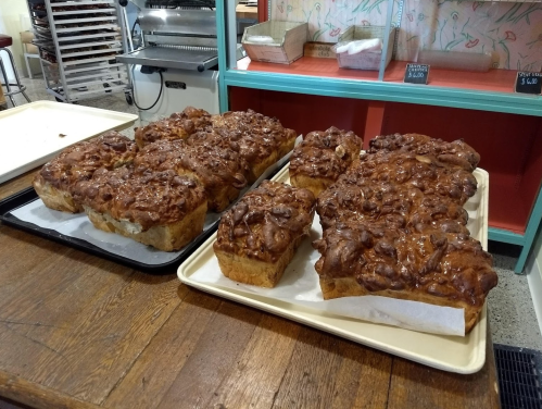 Two trays of freshly baked, golden-brown cinnamon rolls with a glossy glaze, displayed on a wooden table.
