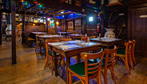 Cozy restaurant interior with wooden tables, chairs, and colorful lights, creating a warm, inviting atmosphere.