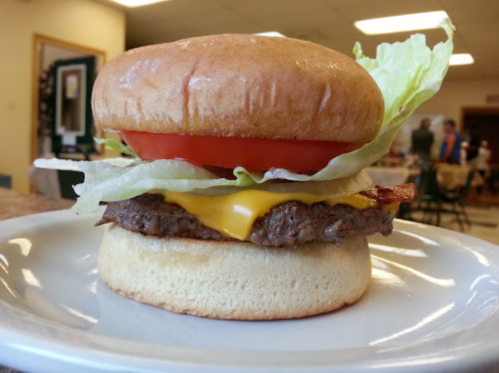A close-up of a cheeseburger with lettuce, tomato, and a beef patty on a soft bun, served on a plate.